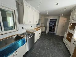 Kitchen remodel in progress with white cabinets, stainless steel appliances, and gray tile flooring.