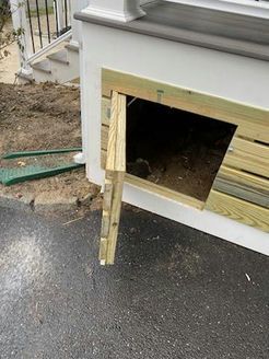 Wooden door open on a white building, revealing a dark storage space, with a driveway and steps in the background.