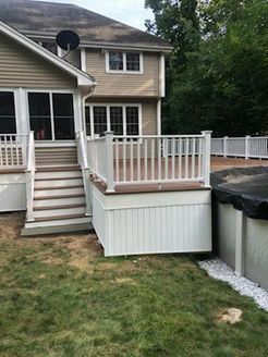 Beige house with a white deck and stairs leading down to a green lawn.