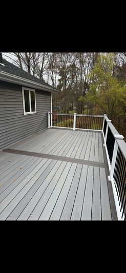 Gray wooden deck with black cable railing next to a gray house, surrounded by trees.