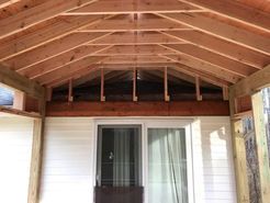 Wooden porch roof framing over a white building with a sliding glass door.