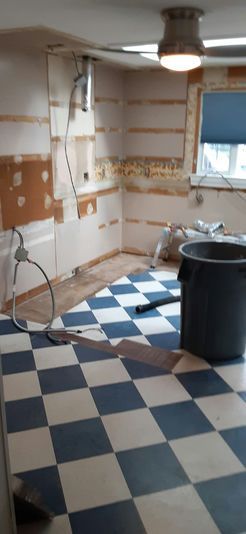 Kitchen renovation in progress: walls stripped, checkered floor, bucket, and light fixture visible.
