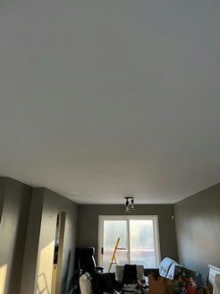 Room interior with gray walls and a ceiling. Window and light fixture visible. Cluttered with objects.