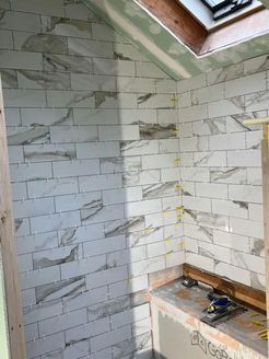 Bathroom with white and gray tiled walls, skylight, and unfinished bench.