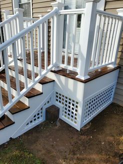 White deck stairs with dark brown steps, lattice side panels, and white railings against a beige siding.