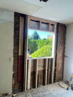 Interior wall with framed window. Window reveals lush green trees and blue sky. Construction in progress.