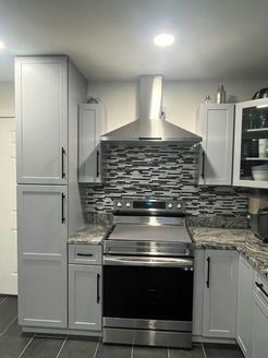 Gray kitchen cabinets with stainless steel oven and range hood; gray and white tile backsplash.
