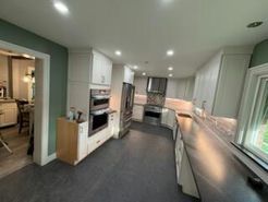 Modern kitchen with white cabinets, stainless steel appliances, dark floor, and a window.