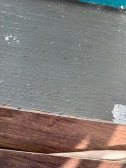 Close-up view of weathered, painted gray wood panel above a darker, wooden strip.