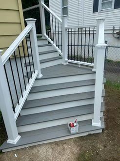Gray composite stairs with white railings and black spindles leading to a house.