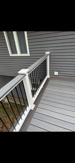 A deck with a grey composite surface and white and black railing next to a grey house.
