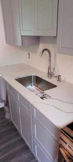 Kitchen countertop with sink and faucet, gray cabinets, white countertop, and gray wood-look floor.