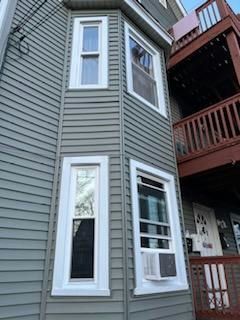 Gray house with bay windows; one window has an AC unit.
