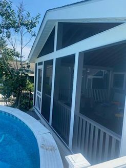 Screened porch with white trim, overlooking a pool. Blue water, trees, and sky visible.