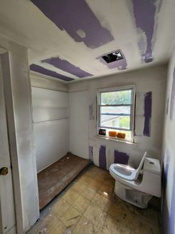 Bathroom under construction; drywall, toilet, window, unfinished ceiling, and floor.