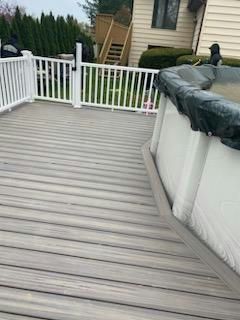 Grey composite deck with white fence surrounds an above-ground pool with a black cover.