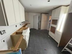 Kitchen under renovation with white cabinets, dark tile floor, and unfinished cabinetry.