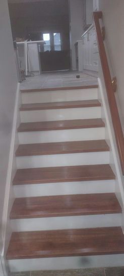 Staircase with wooden steps and white risers, leading to a hallway. Handrail is present.