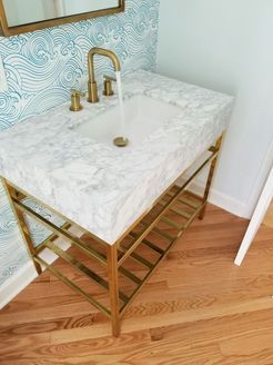 Gold-framed marble-top bathroom sink with a gold faucet. The sink has water running, and a wood floor.