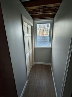 Narrow hallway with closet doors, a window, and gray walls.