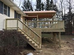 Wooden deck with stairs attached to a house with a covered area.