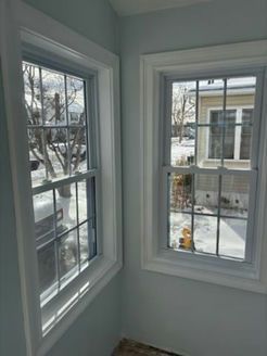 Two white-framed windows on a light blue wall, gridded panes, snow visible outside.