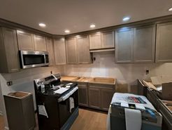 Kitchen under renovation with light-colored cabinets, a stainless steel microwave, and a black stove.