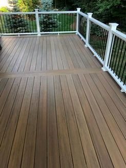 Wooden deck with white railing and black spindles, overlooking a green yard.