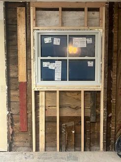 Window installation in progress; new window framed in a wall, studs visible.