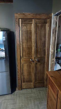 Brown double closet doors with dark stained wooden trim. Beside a refrigerator and part of a wooden dresser.