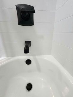 White bathtub with black faucet fixtures against white tiled wall.
