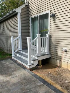A small deck with steps and a white railing leading to a sliding glass door of a house with light brown siding.