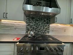 Stainless steel kitchen range with range hood and backsplash.