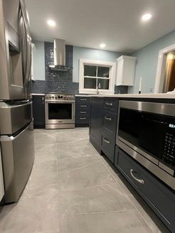 Modern kitchen with stainless steel appliances, blue cabinets, and gray tile flooring.