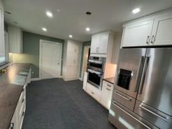 White kitchen with stainless steel appliances, white cabinets, gray floor, green wall.