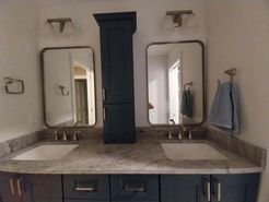 Bathroom with dual sinks, mirrors, and a navy blue cabinet. Light granite countertop, dark blue cabinets, and gold fixtures.
