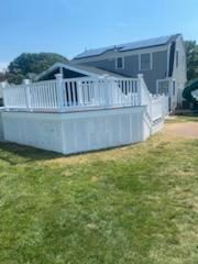 White deck with railing attached to a two-story gray house with solar panels on the roof.