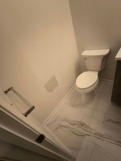 Bathroom with a white toilet, marble-look floor, and a damaged wall with a patch.