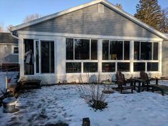 Sunroom addition to a house with large windows, snow on the ground, and outdoor furniture.
