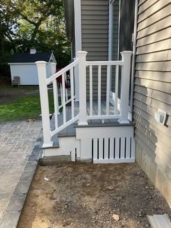 White railing and steps on a home's exterior, next to a gray siding wall and a paved pathway.