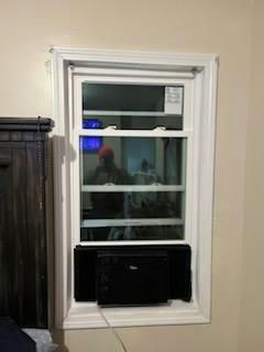 Window with white trim and a black air conditioning unit installed; light tan wall.