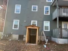 Back of a green building with several windows and a wooden entrance. A ladder leans against the wall.