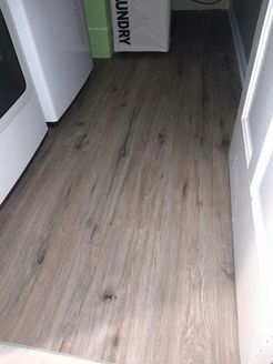 Wooden-look flooring in a laundry room, between a white washing machine and a white door frame.