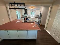 Kitchen remodel: white cabinets, dark countertops covered in red paper, black range hood, and new flooring.