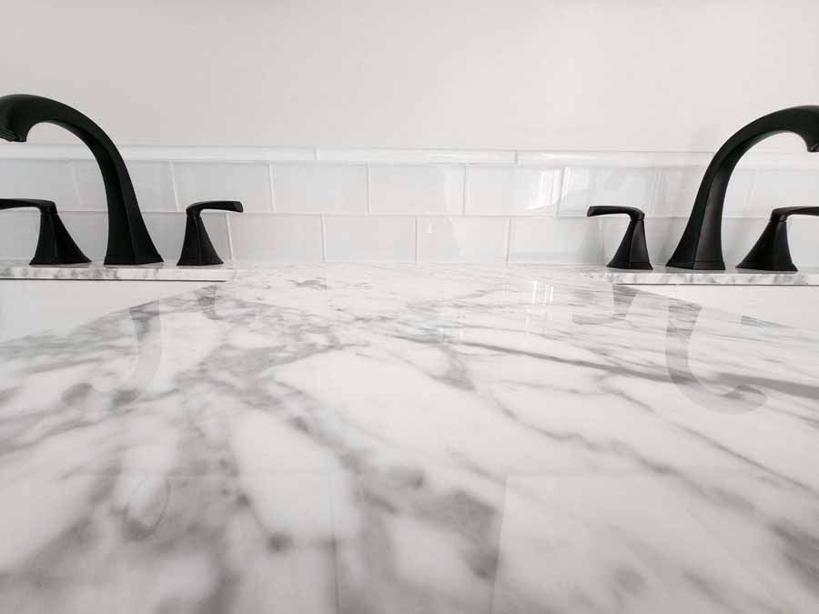 White marble countertop with black faucets, white tile backsplash.