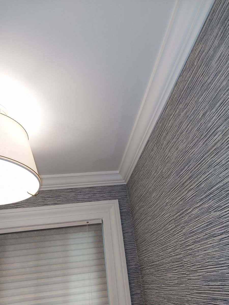 White ceiling, crown molding, patterned wallpaper, window with blinds.