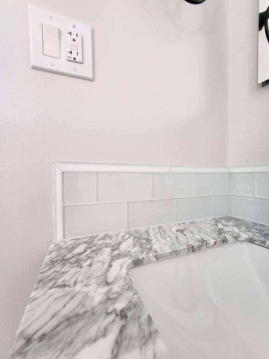 White bathroom counter with marble pattern, white tile backsplash, and light switches on a white wall.