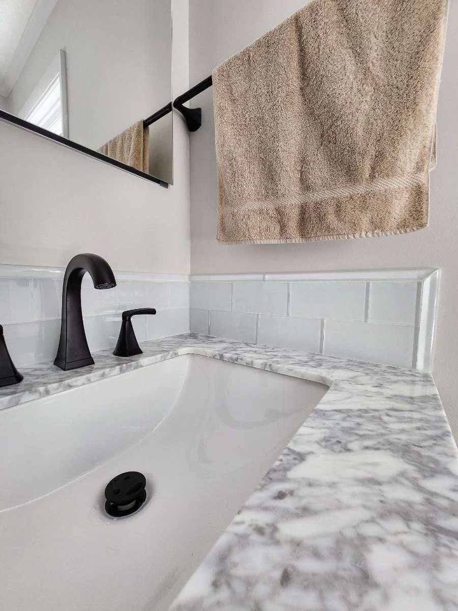 Bathroom sink with marble countertop, black faucet, and tan towel hanging above.