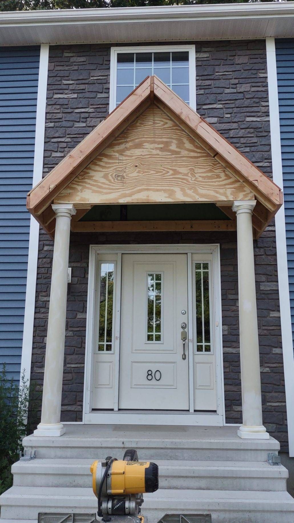 Blue house front entrance with stone accent, white door, and unfinished wooden porch.