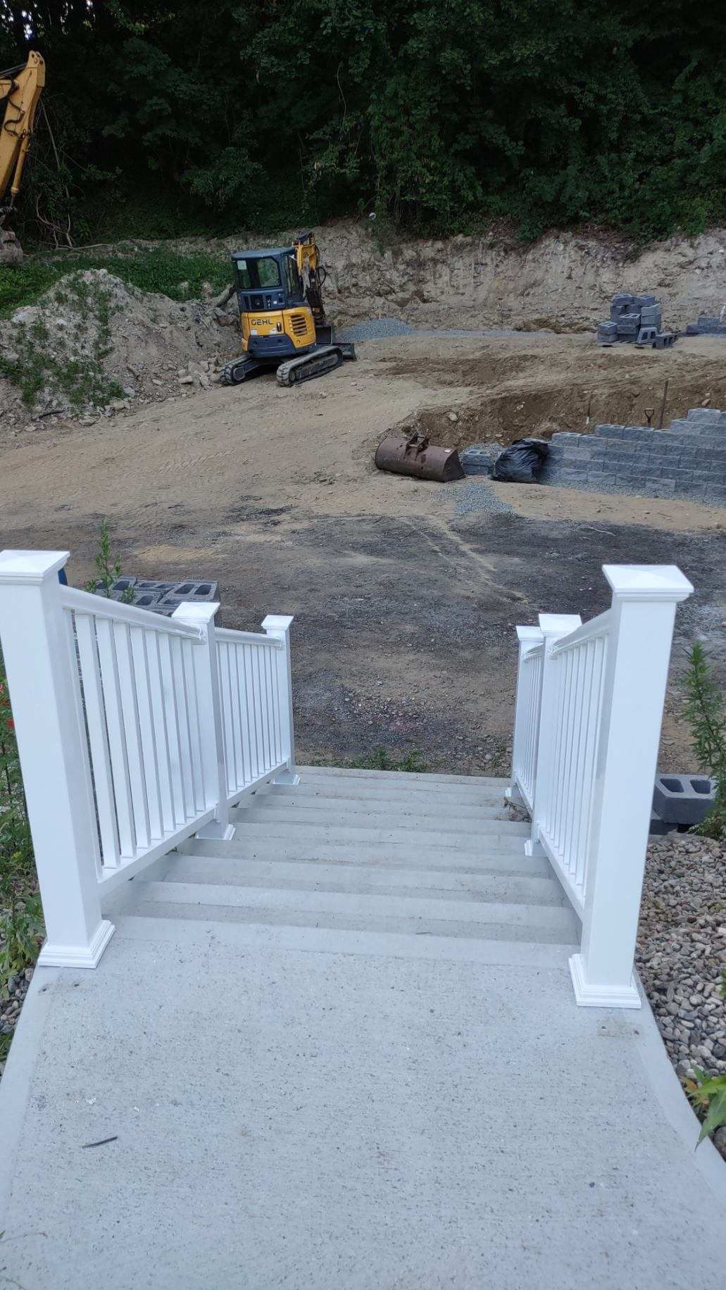 Concrete stairs with white railings lead down to a construction site with an excavator.